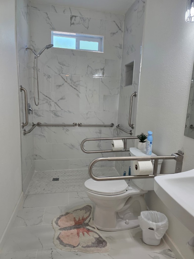 Walk-in shower with marble tile, grab bars, and an accessible toilet
