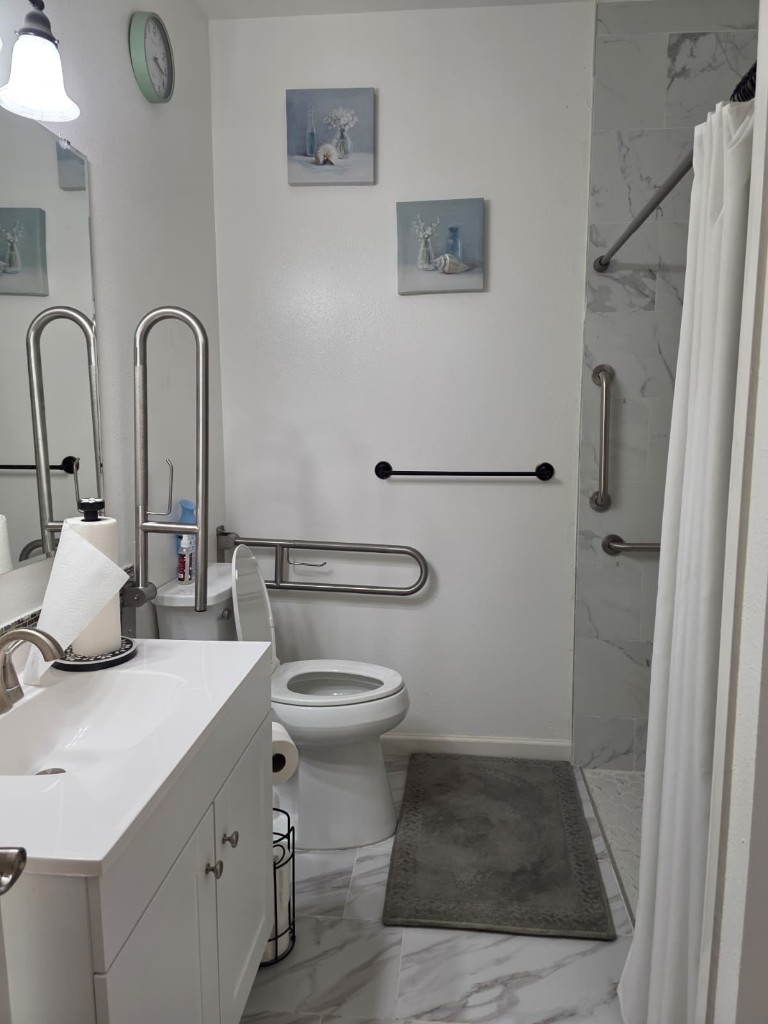 Resident bathroom with a white vanity, grab bars, and a walk-in shower
