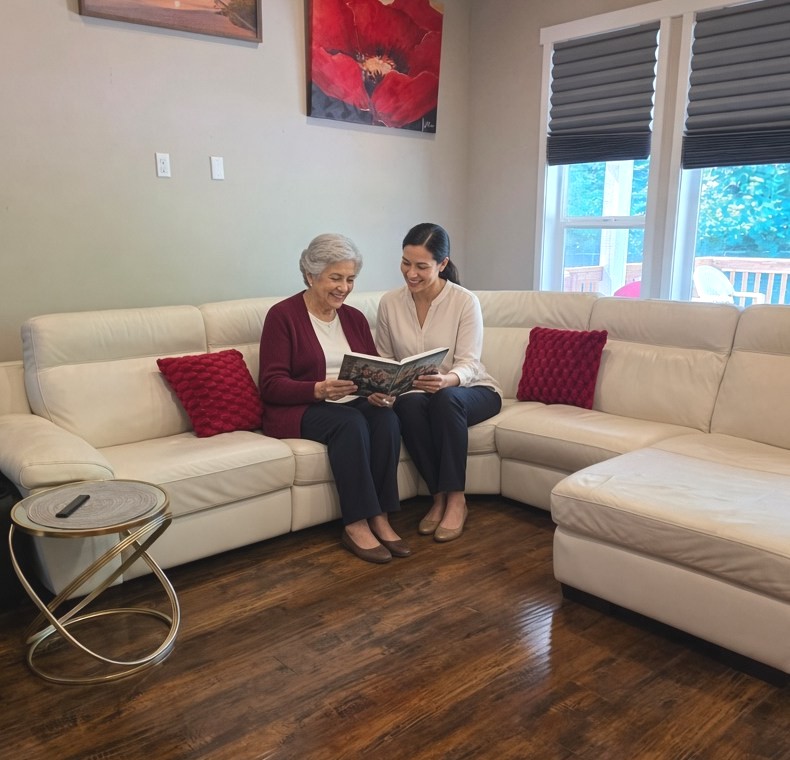 A caregiver and an older woman looking through a photo album on the sofa