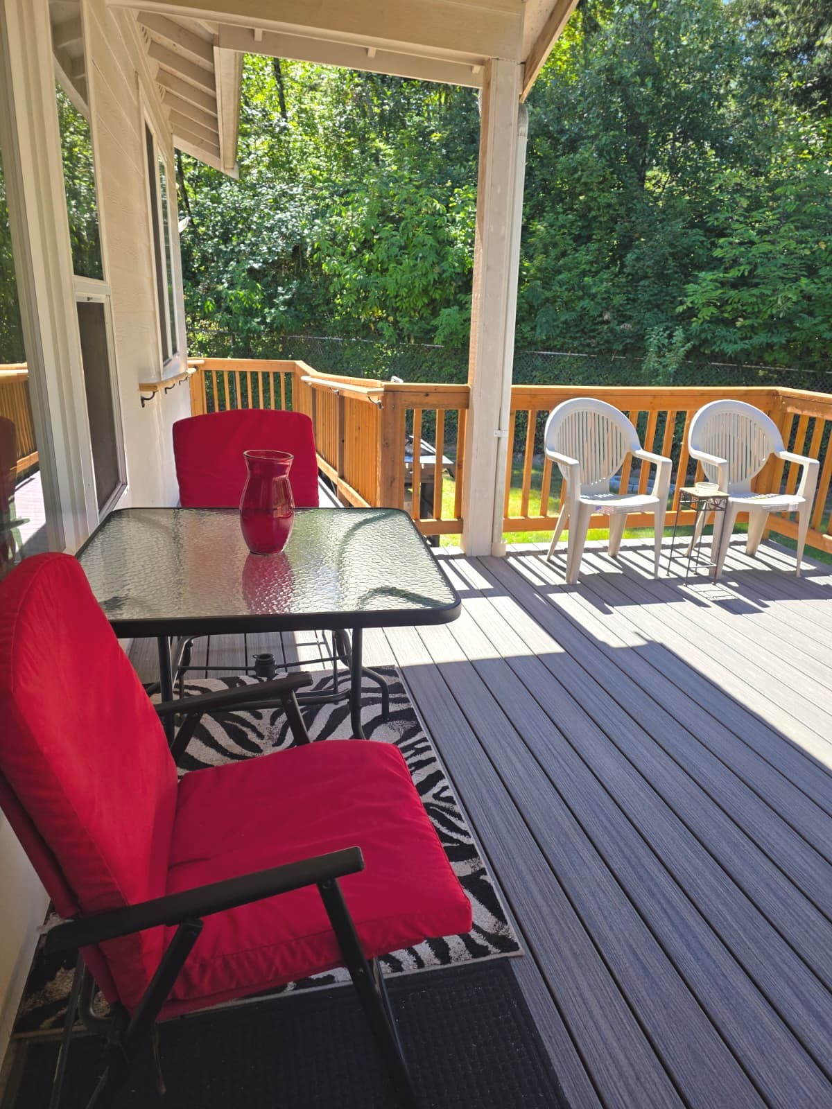 Sunny outdoor deck with seating surrounded by green trees at Adalena 2